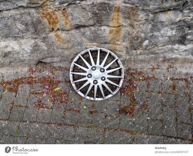 Lost silver hubcap in the style of a light alloy rim on old grey pavement in front of natural stone masonry in Oerlinghausen near Bielefeld in the Teutoburg Forest in East Westphalia-Lippe
