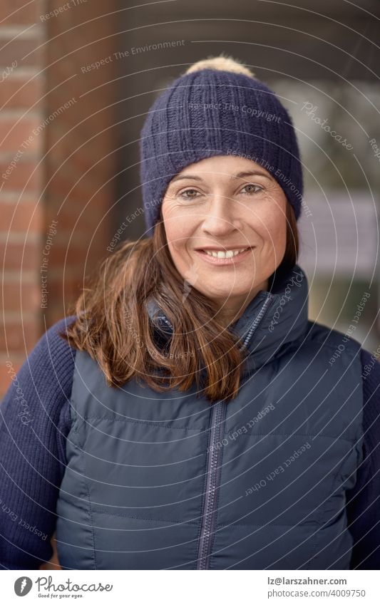 Attractive friendly smiling woman in blue winter outfit with knitted beanie hat and warm jacket in a close up head and shoulders outdoor portrait face fashion