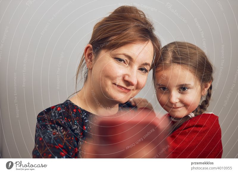 Mother with her little daughter making video call using mobile phone. Woman and little girl talking with relatives. Cheerful family having fun taking selfie photo using smartphone