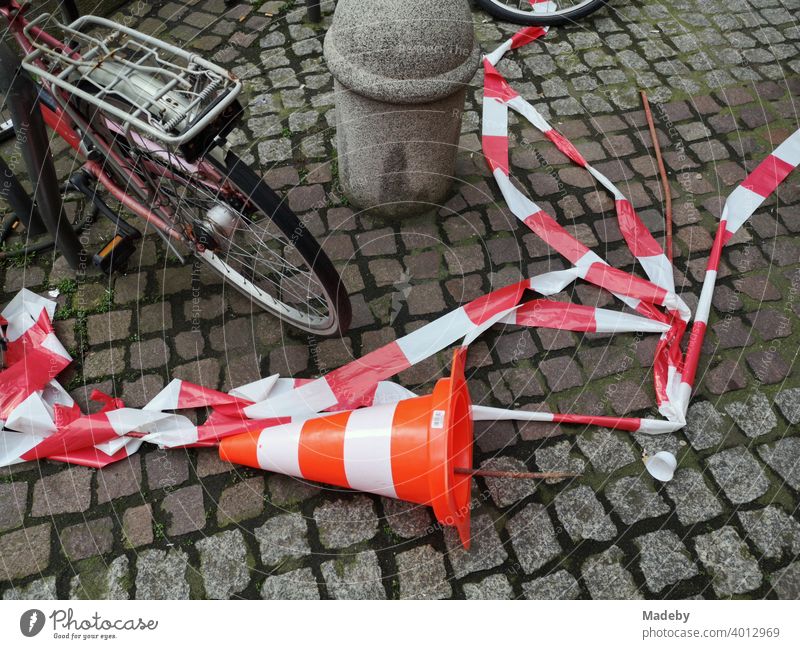 Overturned Lübeck hat and torn red and white barrier tape on cobblestones in the city centre of Frankfurt am Main, Hesse Lübeck cone Skittle Traffic cone cordon