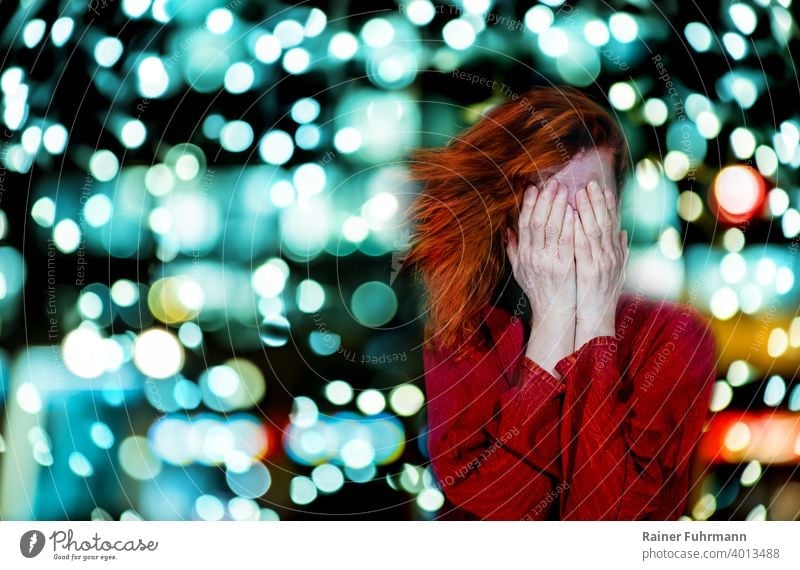 A red-haired woman holds her hands in front of her face. The bokeh of bright lights shines in the background. Woman problems clearer Headache Abstract