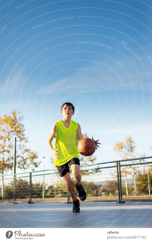 Cute boy in yellow shirt plays basketball on city playground. player teenage male training outside teenager bouncing sport outdoor competition game person