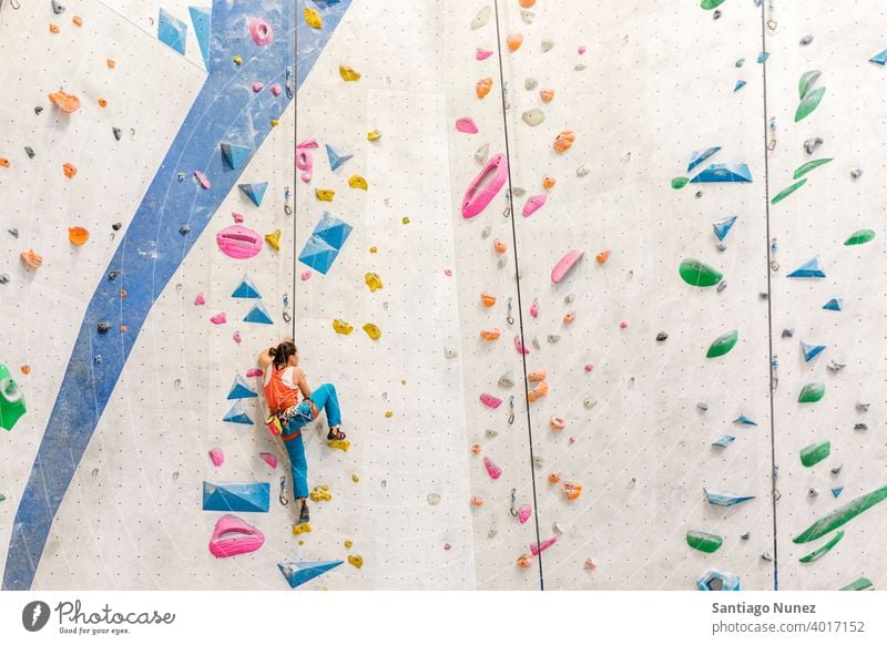 Beautiful young woman in black outfit climbing on practical wall in gym,  bouldering, extreme sport, rock-climbing concept Stock Photo