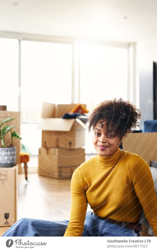 Portrait Of Young Woman Sitting On Floor And Smiling As She Moves Into New Home Surrounded By Boxes woman house buying unpacking boxes home new home first home