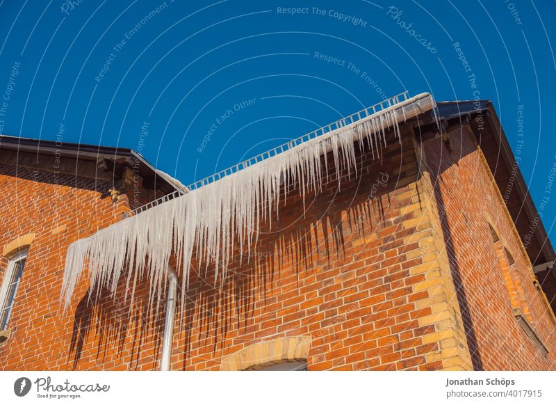 lange Eiszapfen an Dachrinne eines Backstein Haus im Winter bei eisiger Kälte und Sonne Architektur Backsteinhaus Backsteinhaussiedlung Dachkante