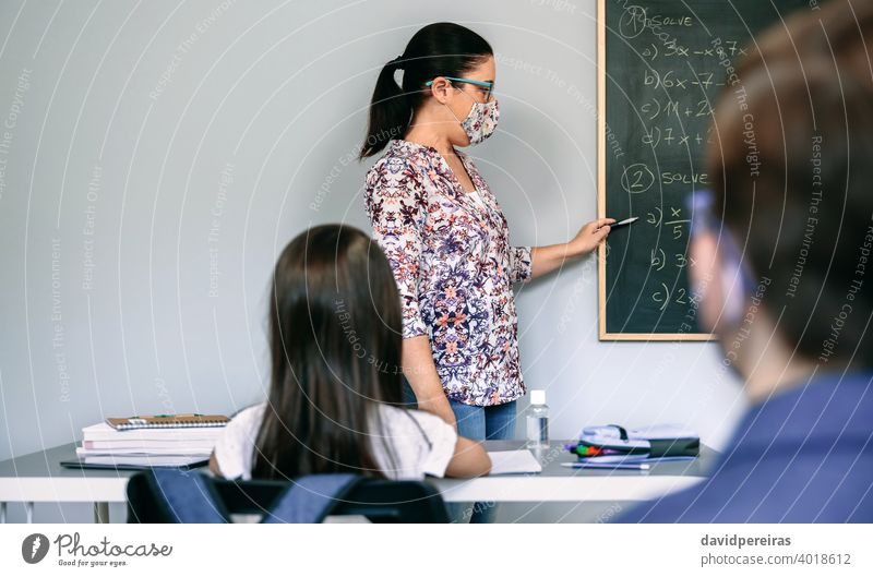 Teacher with mask explaining exercises in math class female teacher protective mask new normal student covid-19 blackboard school pointing copy space safety