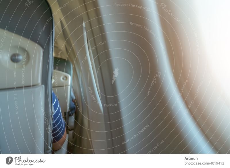 Rearview of airplane seat near plane window. Economy class airplane. Inside of commercial airline. Small space between passenger economy seat and window of airplane. Seat with armchair. Leather seat.