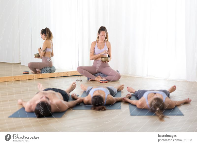 Restorative yoga. Group of young sporty attractive people in yoga studio, lying and relaxing on yoga mats during restorative yoga session. Healthy active lifestyle.