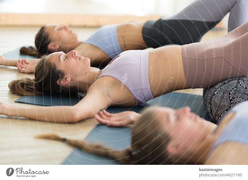 Restorative yoga with a bolster. Group of three young sporty attractive women in yoga studio, lying on bolster cushion, stretching and relaxing during restorative yoga. Healthy active lifestyle
