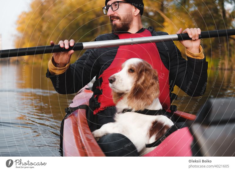 Happy man rowing a canoe with his spaniel dog, sunny autumn weather. Going kayak boating with dogs on the river, active pets, wholesome dog and owner on an adventure