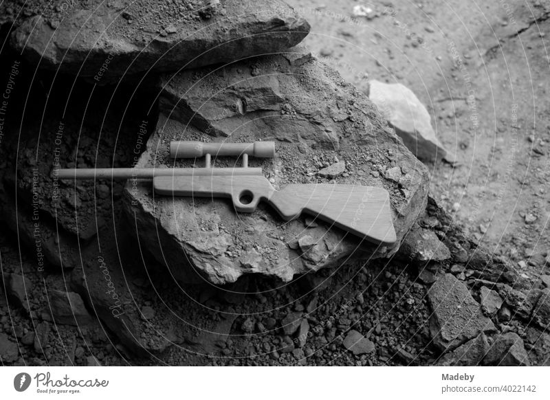 Toy rifle made of wood with telescopic sight on crumbling rock of an old farmhouse in Rudersau near Rottenbuch in the district of Weilheim-Schongau in Upper Bavaria, photographed in classic black and white