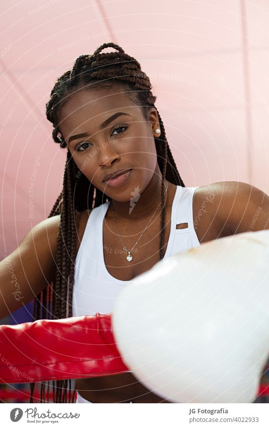 Portrait of beautiful young afro american woman looking at camera wearing boxing gloves inside boxing ring in a gym. training sports beauty female wellness body