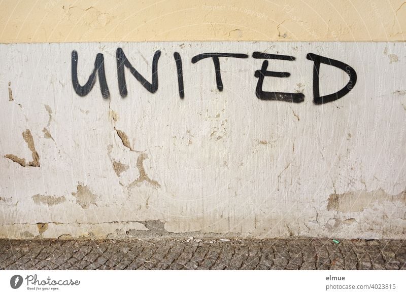 "UNITED" is written in black capital letters on the gray, old, plastered wall / connected / scrawl. united Wall (building) interconnected Facade Password