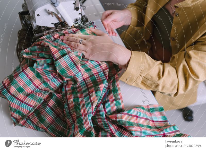 Top view of woman working on overlock sewing machine in her workshop, clothing material fabric creative thread sitting tool tailor industry equipment fashion