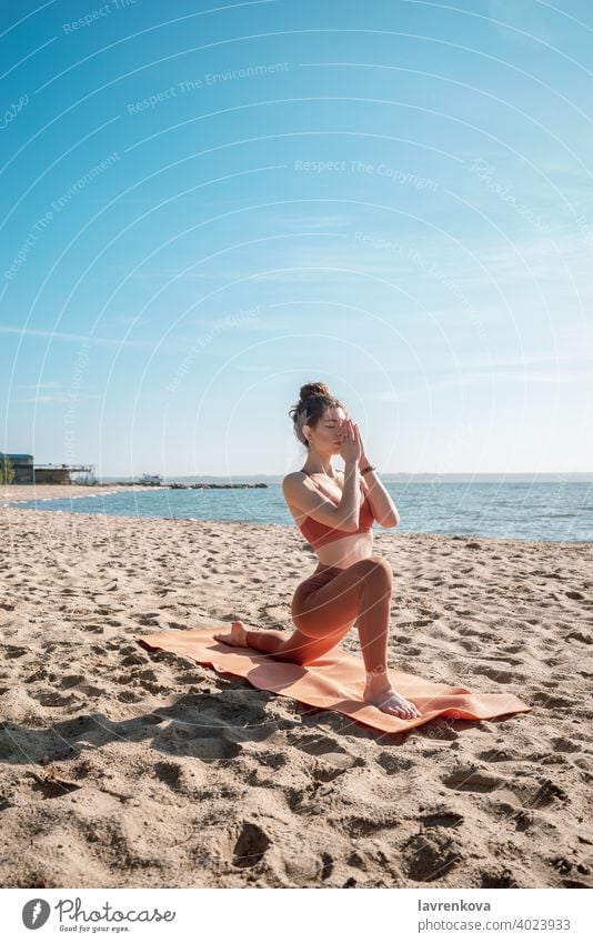 Young female in orange top and leggins practising Crescent Lunge Pose (Anjaneyasana) on a beach in the morning woman exercise pose yoga young practicing outdoor