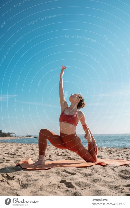 Young female in orange top and leggins practising Crescent Moon Pose (Anjaneyasana Variation)  on a beach in the morning woman exercise pose yoga young