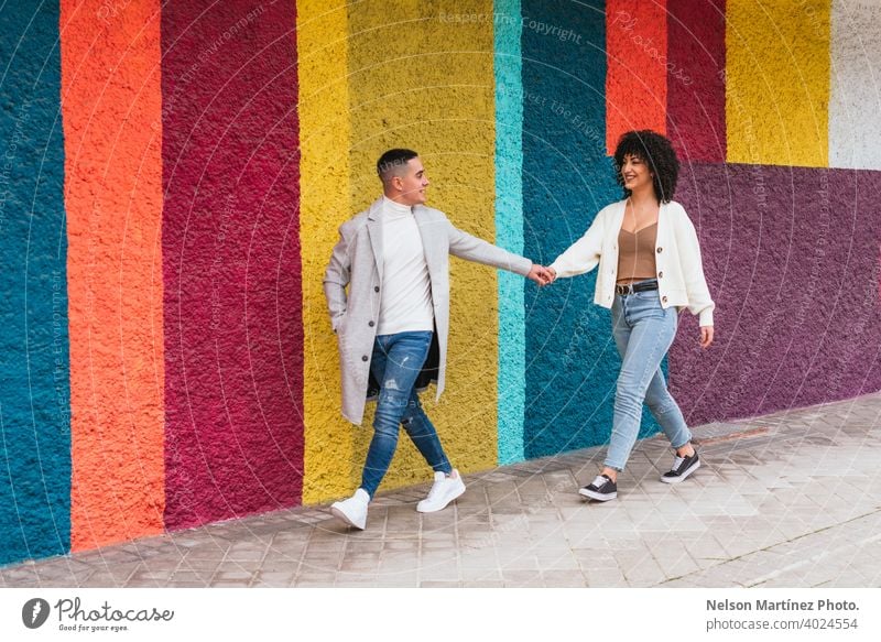 Young happy couple holding hands and walking through a pavement against a colorful wall stripes young love woman people together male relationship two happiness
