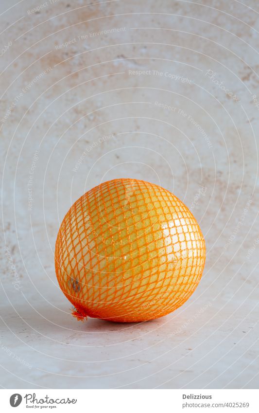 pomelo, single wrapped in a net and plastic foil on neutral background, vertical with copy space asian asian fruit citrus citrus maxima closeup delicious detox