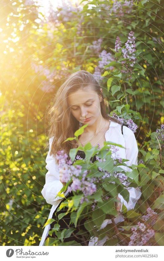 unreal stunning beautiful young woman walking in a green flowered in spring in a lavender garden with a bouquet of lilac in the hands. Closeup fashion romantic portrait. smelling the flowers