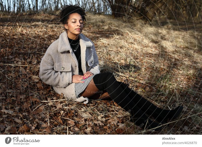 Young woman in fur jacket and skirt sits in nature sunbathing Woman Athletic Dark-haired Long-haired pretty Strong Graceful naturally Curly Slim Nature by