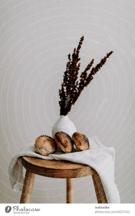 Three sourdough bun with poppy seed and sesame on a napkin on a wooden stool, and dried wild flower at the background breakfast bread gluten bread roll pastry