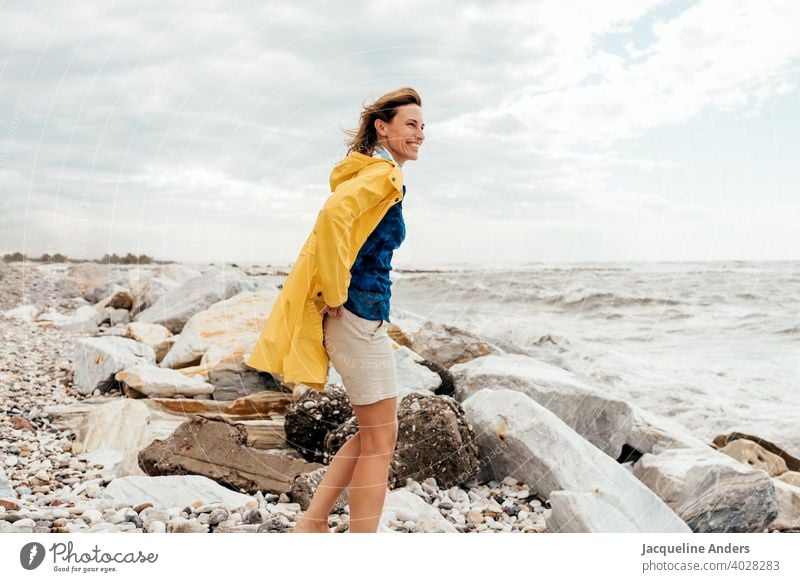 Woman with blowing hair in a yellow raincoat looks at the sea Ocean Seashore Wind Raincoat Yellow hair in the wind fortunate Summer Nature Freedom