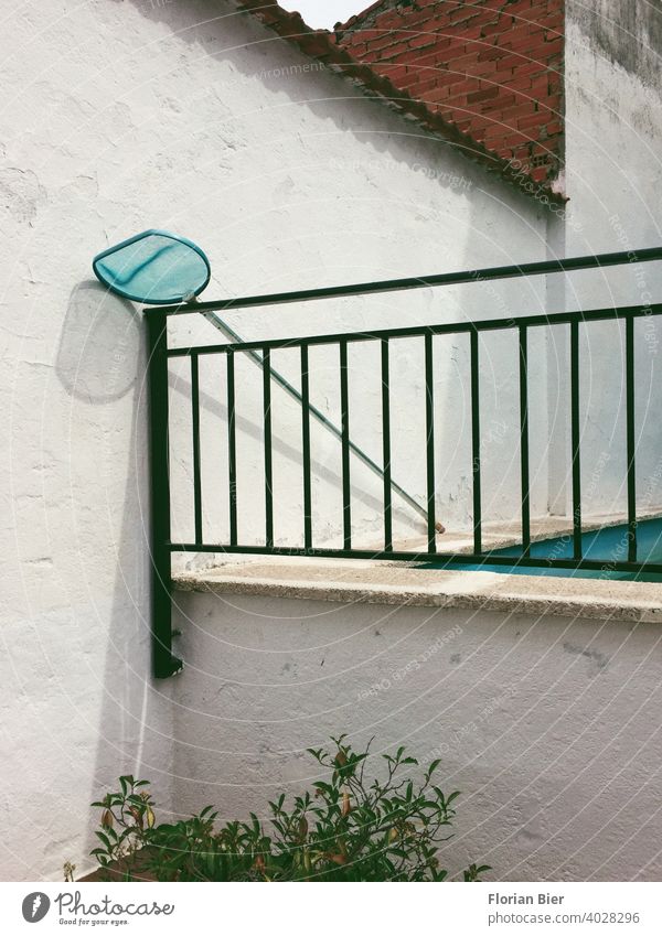 Pool landing net leaning against an iron railing next to a swimming pool in the backyard Landing net Backyard Swimming pool Wall (barrier) brick Wall (building)