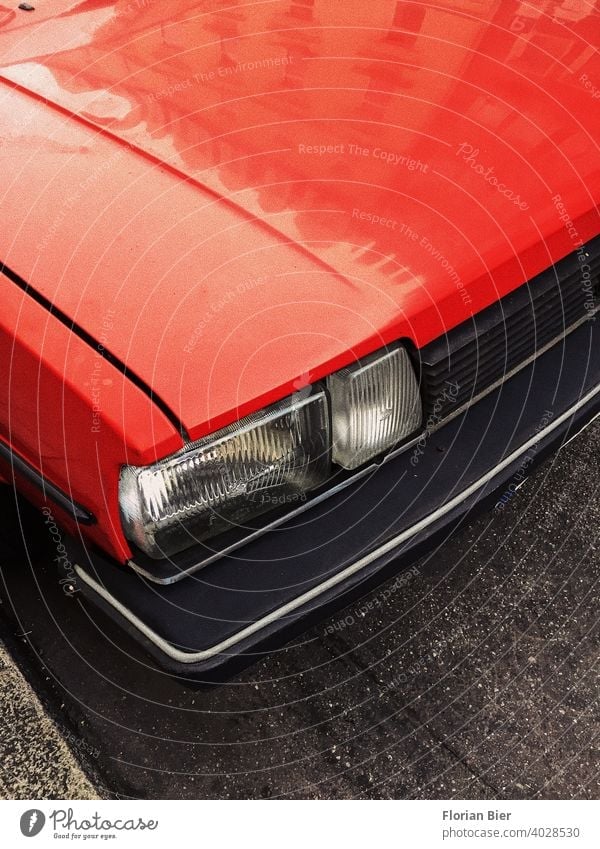 Red painted bonnet and angular headlight as well as radiator grille and plastic bumper of a parked car on the street Car Hood Floodlight transparent Bumper