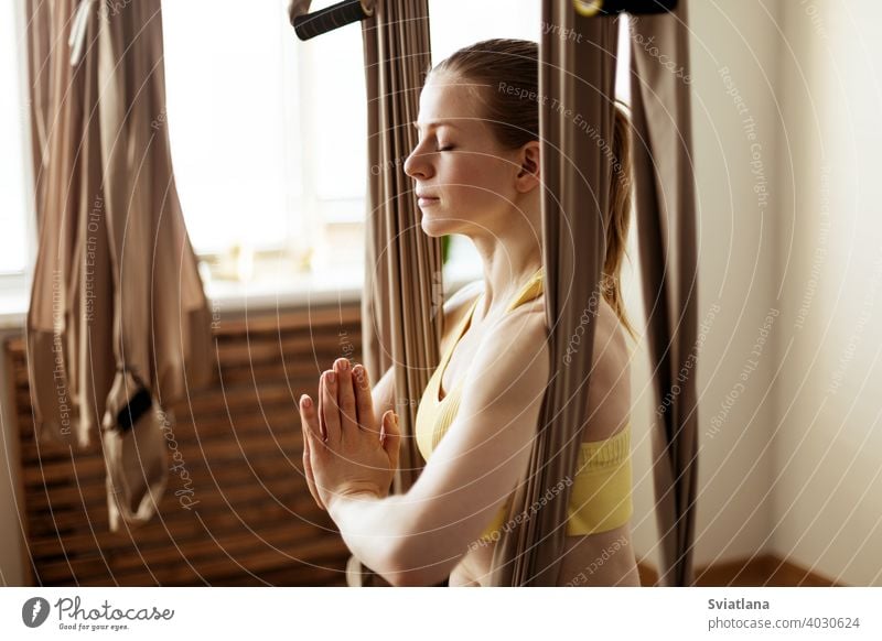 A young woman meditates in a hammock after an aero yoga class. Yoga-meditation in a hammock. Healthy lifestyle and relaxation concept fitness girl club stretch
