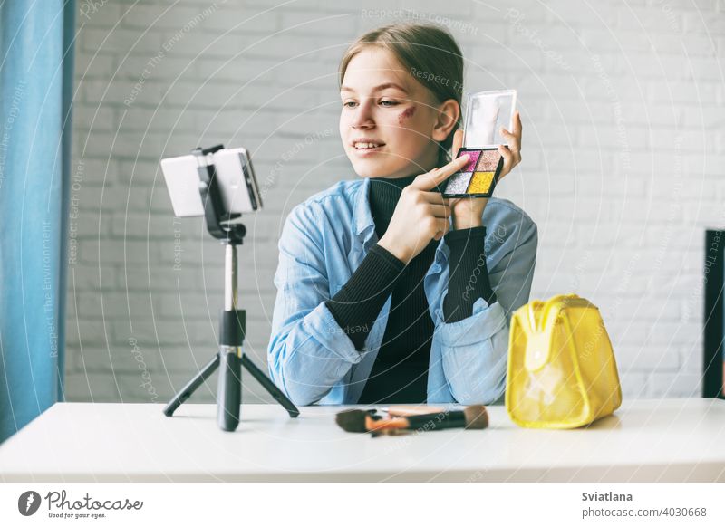 A teenage girl does makeup and shows how to apply blush while recording video for her blog on her smartphone on a tripod at home blogger camera cosmetics