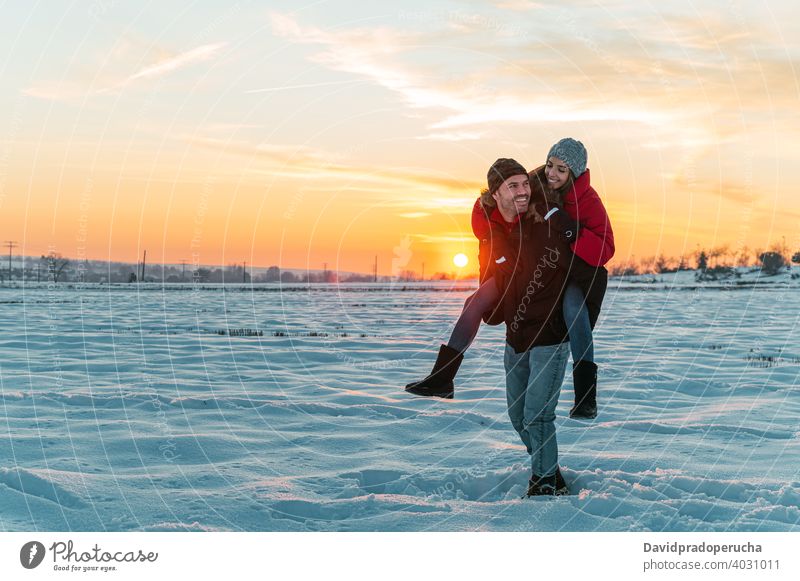 Happy couple having fun in snowy field piggyback winter cheerful countryside love together ride joy laugh romantic relationship affection excited fondness