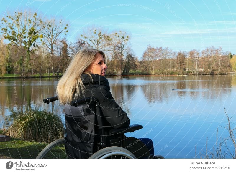 Concept of disabled person. A woman in a wheelchair outside in the nature in front of a lake. adult beautiful blonde hair caucasian concept contemplation