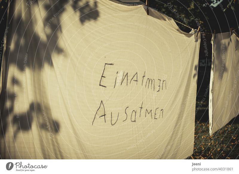 "EINATMEN AUSATMEN" on a bed sheet on a clothesline with shadows cast by a tree in low sun | corona thoughts Inhalation exhale Breath Breathe Air Breathe in