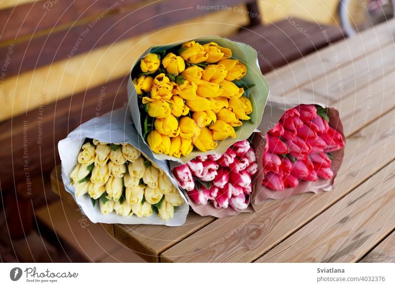 Several bouquets of tulips of different colors in paper packaging lie on a wooden table. Women's Day, Mother's Day, Valentine's Day. A gift, greeting card, place for text