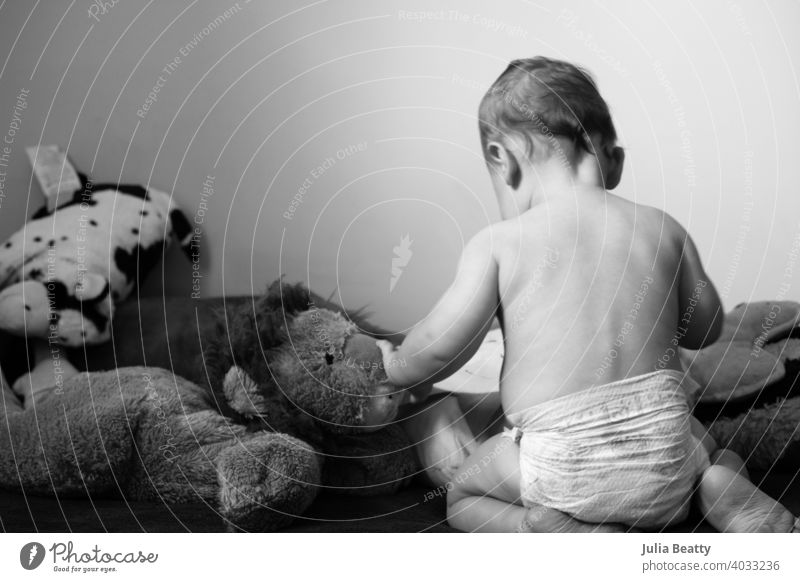 Young baby sits up in bed with stuffed animal toys; child wearing diaper 6 months old sitting up seated back spine hair reach touch stuffed animals lion