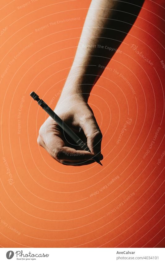 A young hand grabbing a mechanical pencil over a orange background with deep shadows office design paper education drawing business tool school isolated write