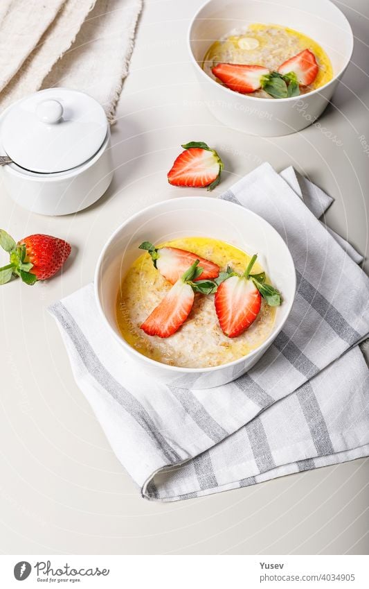 Classic oatmeal with butter and fresh fruit. Sweet strawberries. Delicious and healthy breakfast. Food still life on a light background. Ideas and recipes for home meals. Vertical shot