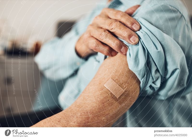 Senior man patient holding shirt sleeve up with a plaster in place of injection of vaccine. Covid-19 or coronavirus vaccination person hospital senior medical