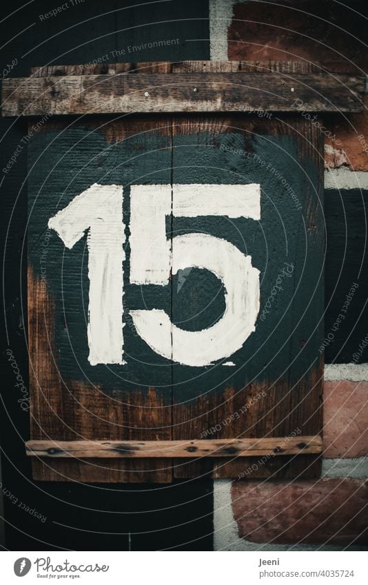 House number fifteen written as number 15 on rustic wooden board with white paint on dark background Digits and numbers digit Numbers and numbers