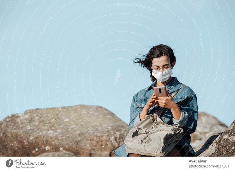 A young woman wearing a mask checking his phone while the wind blows with copy space female mobile people nature person smiling happy beautiful cellphone