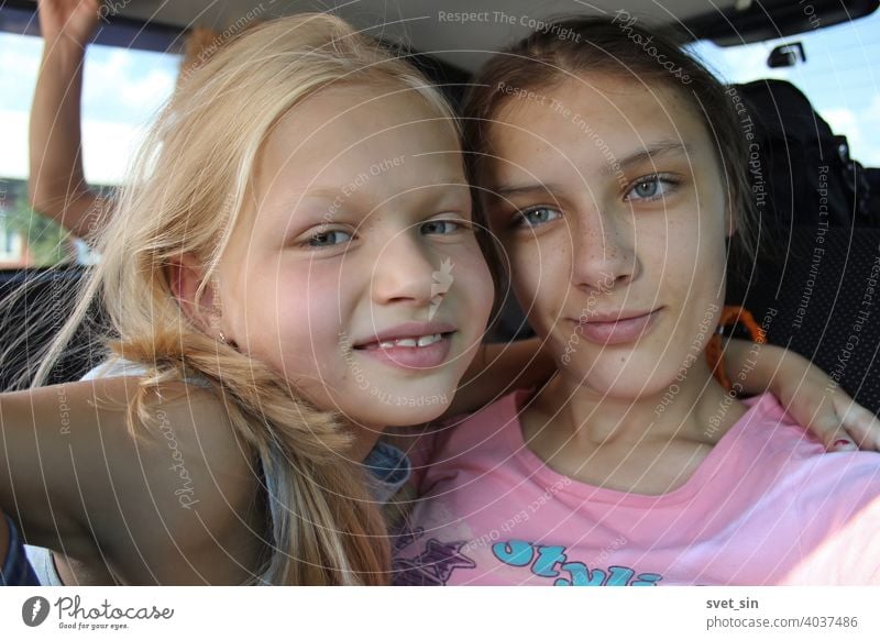 Smiling sisters on a car trip: blonde and brown-haired. Two girls of different ages are smiling, hugging each other, inside the car. teenage laugh emotion
