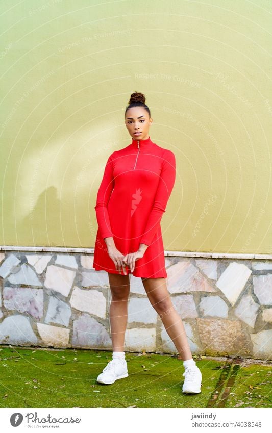 Young mixed woman in red dress with a serious expression in urban background. black bow hairstyle model beauty fashion pretty portrait girl young female person