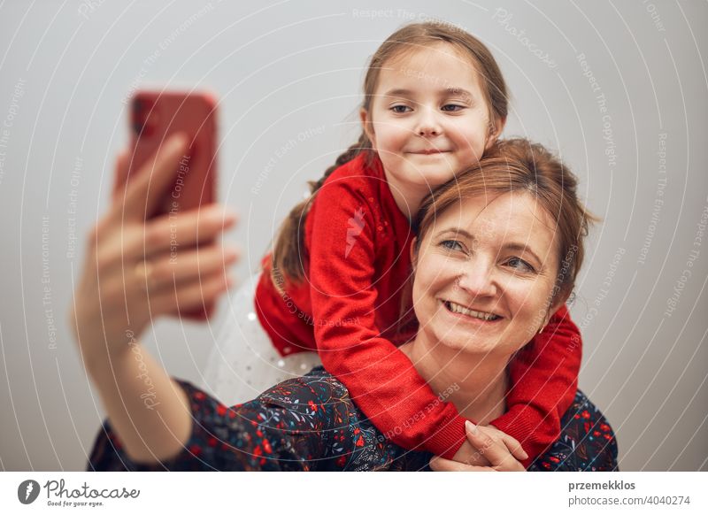 Mother with her little daughter making video call using mobile phone. Woman and little girl talking with relatives. Cheerful family having fun taking selfie photo using smartphone