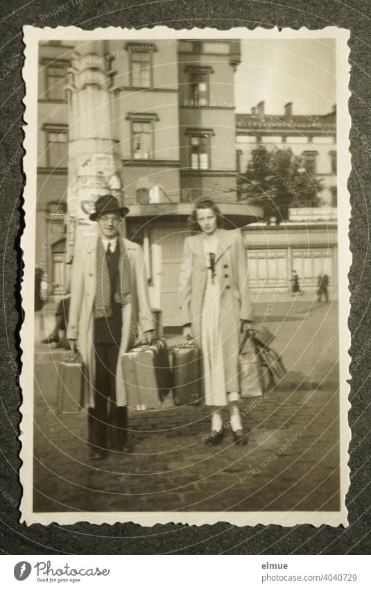 Black and white photo with deckle edge from the 1950s on a black photo album page, showing a young couple with travel suitcases / holiday trip / memories / analog photography