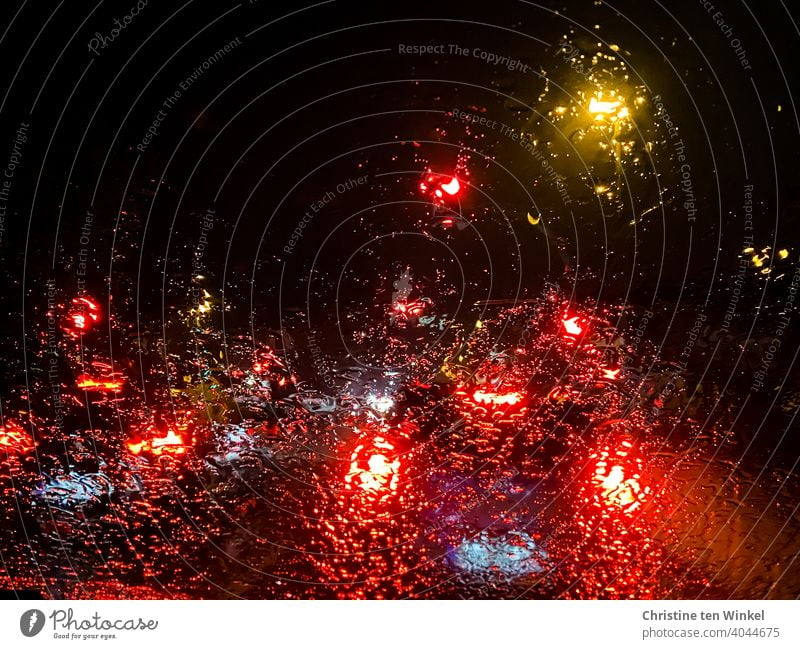 View through the rainy windscreen of a car parked at a red light in the darkness behind illuminated vehicles clearer Lights in the rain Rain Car lights Wet