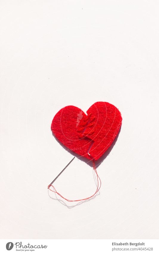 broken red heart (made of felt) on a white background, sewn back together with needle and thread. Lovesickness broken heart heartache Heart