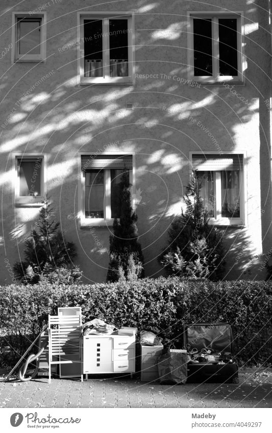 Old furniture and utensils in front of a hedge and an apartment building in summer sunshine in the West End of Frankfurt am Main in Hesse, photographed in classic black and white