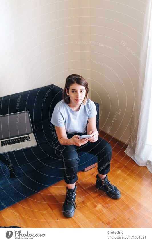 Girl typing on the cell in her sofa with her winged laptop person woman happy young couch home female technology communication sitting message room caucasian