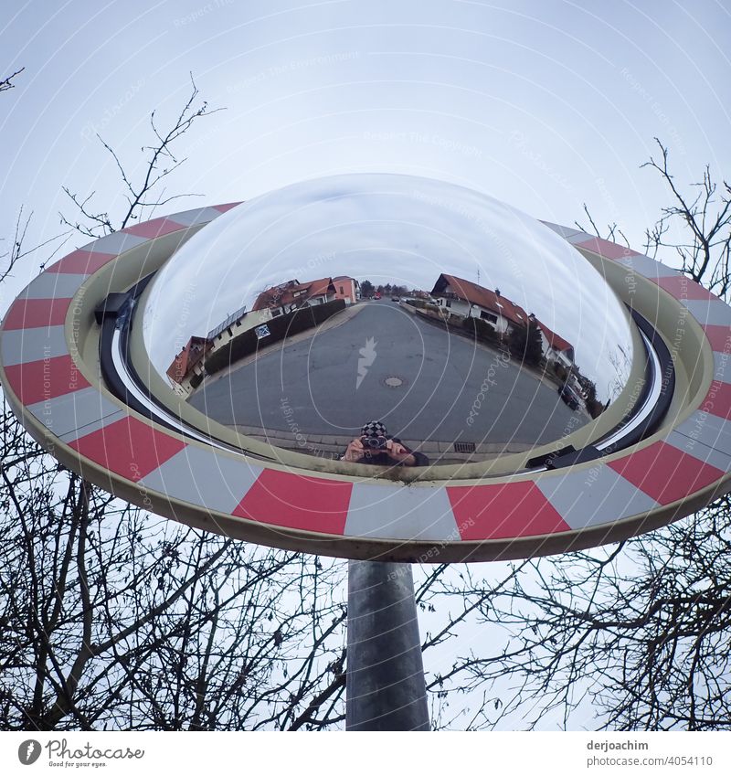 Traffic mirror with view to the right left. In the background is the street with houses. At the bottom of the mirror very small, the photographer. Mirror Street