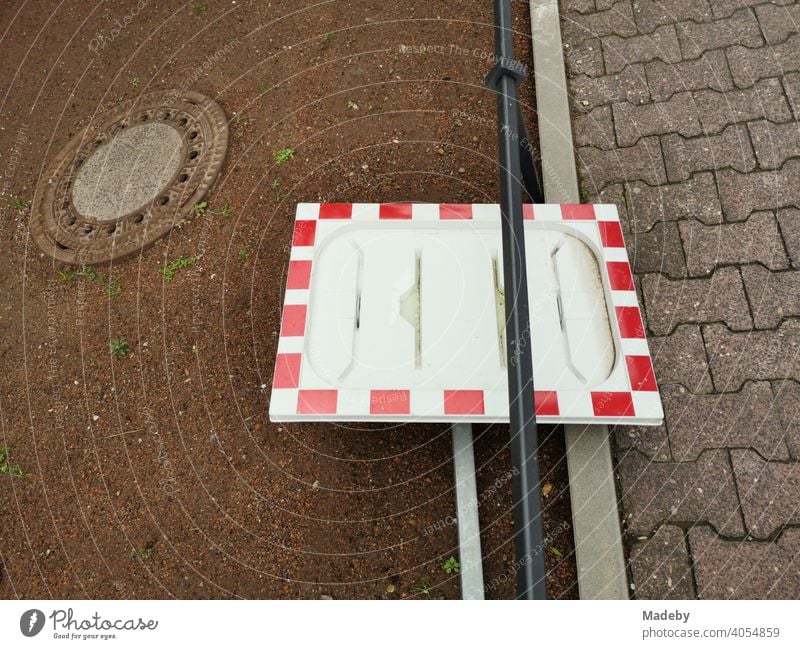 Frame of a traffic mirror in red and white without mirror as still life with manhole cover at the roadside in the district Bockenheim in Frankfurt am Main in Hesse